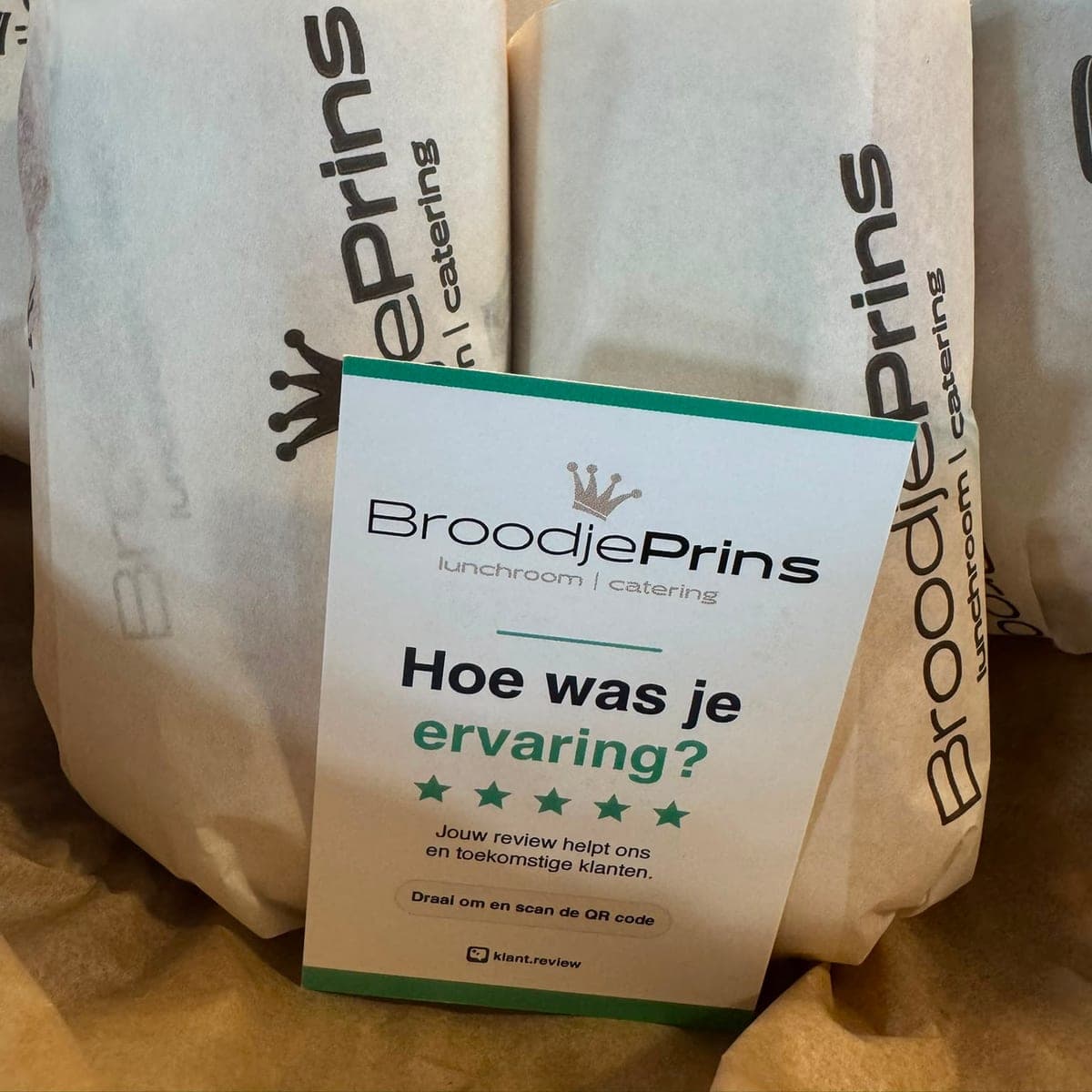 Reviewkaartje met QR-code van lunchroom BroodjePrins tegen ingepakte broodjes, voorkant met logo, de vraag Hoe was je ervaring en vijf groene sterren