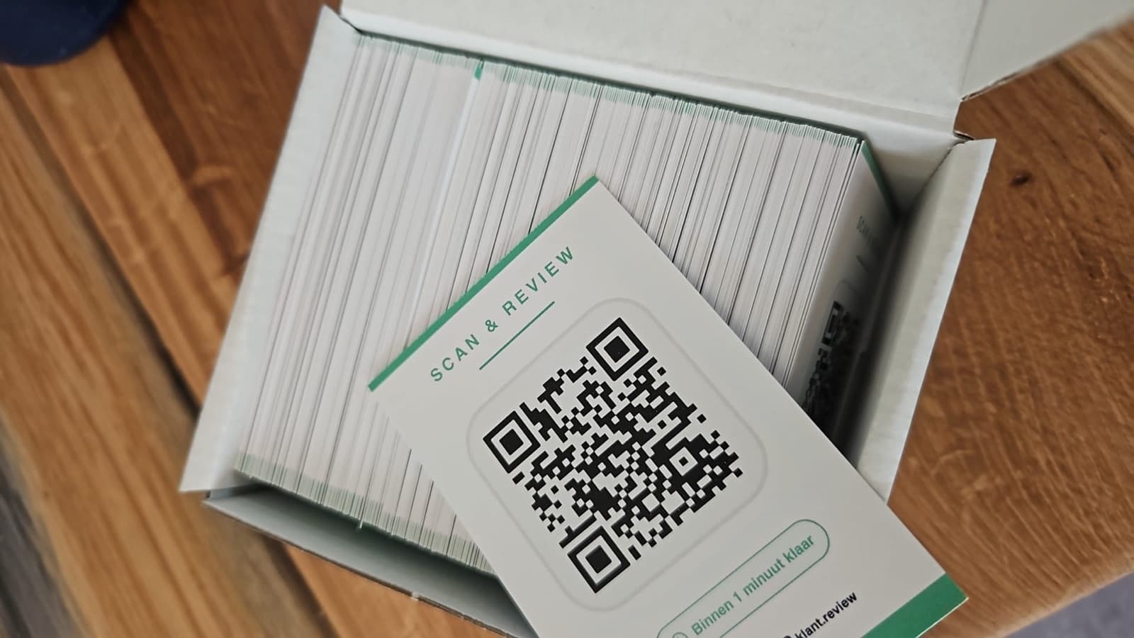 Geopend doosje met een stapel gedrukte reviewkaartjes, met bovenop een kaartje met de tekst Scan en review en een QR-code